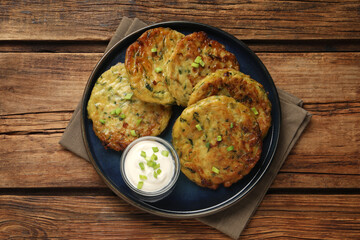 Delicious zucchini fritters with sour cream served on wooden table, top view