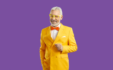 Studio shot of happy white haired bearded senior man wearing bright yellow suit, white shirt,...