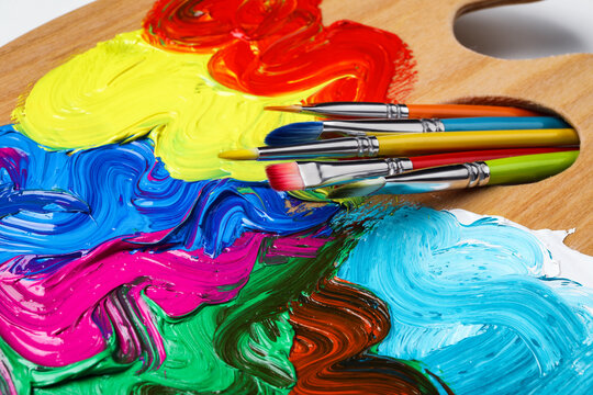 Palette with colorful acrylic paint and brushes on white background, closeup view