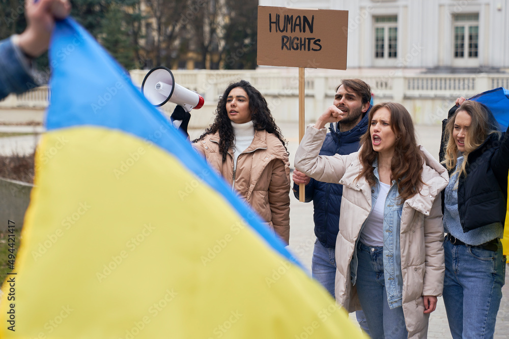 Wall mural Ukrainian flag and group of young caucasian people manifesting against Ukrainian war