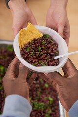 Vertical from above shot of unrecognizable volunteer giving bowl with meal to cash-strapped person in charity canteen