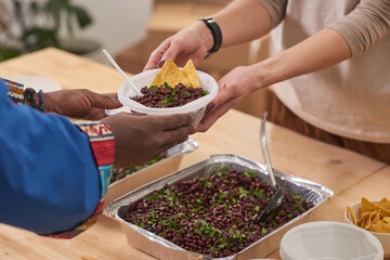Unrecognizable volunteer giving bowl with nutritious meal to poor African person in modern charity canteen