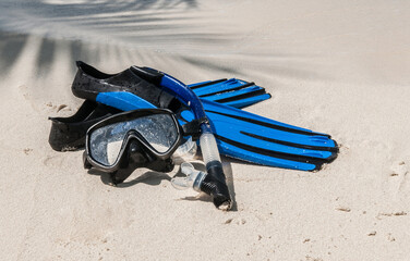 Mask and fins for scuba diving and snorkeling lie on the sandy shore against the backdrop of the sea and ocean. - obrazy, fototapety, plakaty