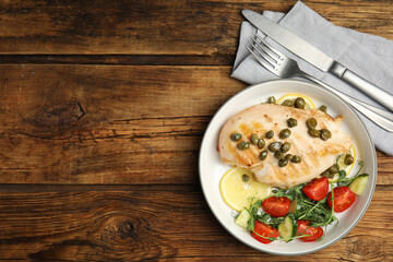 Delicious cooked chicken fillet with capers and salad served on wooden table, flat lay. Space for text