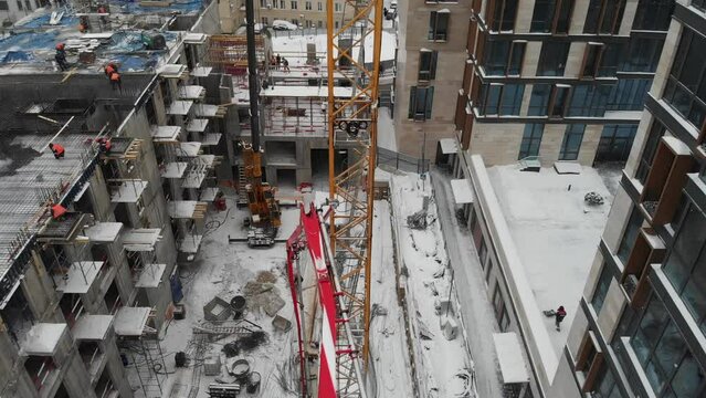 construction of a residential building in the city center using a tower crane and a concrete pump truck, winter day