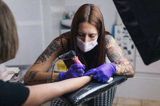 Female tattooist tattooing with mask and gloves. Tattoo art on body. People, lifestyle.