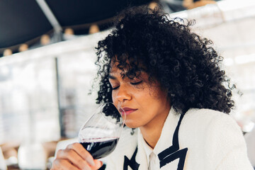Woman sommelier tasting a glass of red wine in a wine cellar. Elegant woman in her 30's smelling...