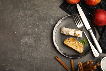 Delicious strudel, cinnamon and fresh apples on grey table, flat lay. Space for text