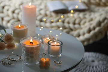 Burning candles, flowers and jewelry on table in room