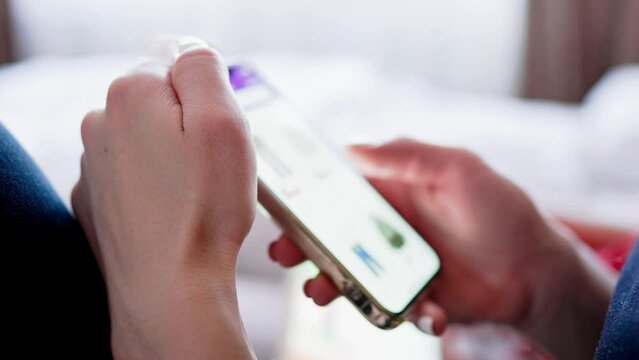 Online shopping concept. Young woman sitting on the bed and makes online shopping on a smartphone. Woman at Home Lying on Couch in Living Room Using Smartphone Buys in Internet Shop.