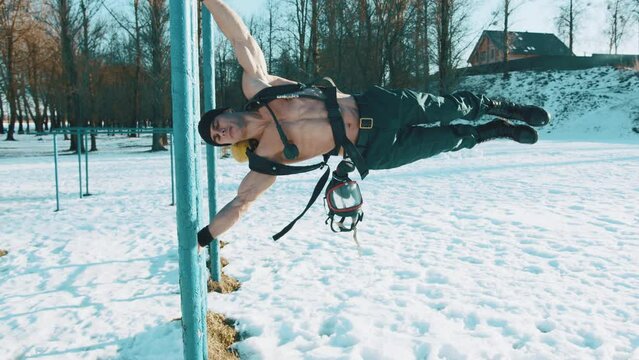A young muscular man with a drager on his back does the exercise horizon in a winter park and pretends to be striding