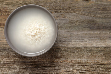 Bowl with rice soaked in water on wooden table, top view. Space for text