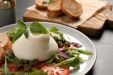 Delicious burrata salad with tomatoes, arugula and pesto sauce on dark grey table, closeup