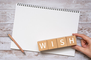 「WISH」と書かれた積み木とノートとペンと人の手