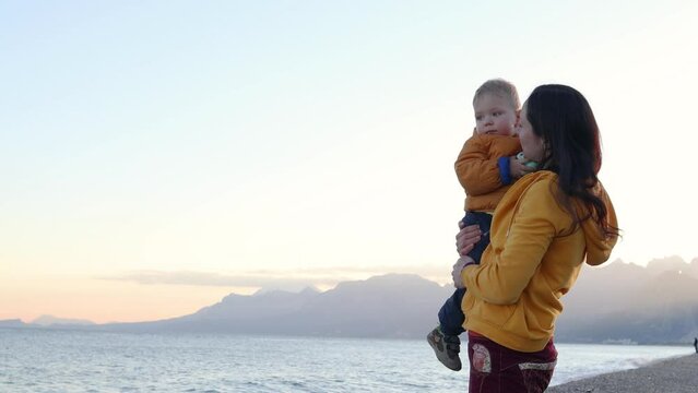 A woman with a child walks along the sea coast, a mother hugs her son, a boy and mother look at the sea waves