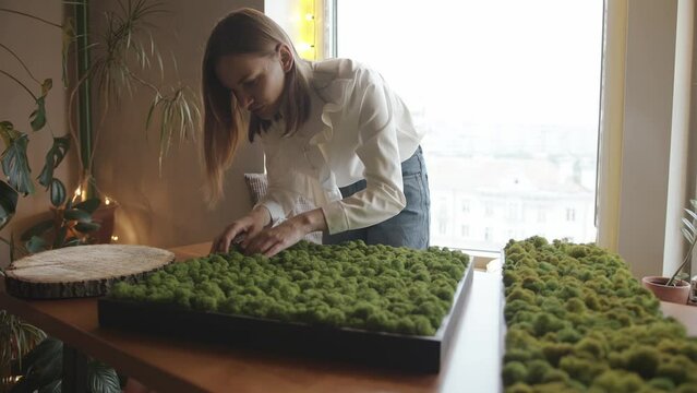 A pleasant young girl takes from the table a small wooden box with decorative moss and sniffs it. Interior decor concept. Slow motion