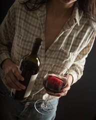 A woman with a plaid shirt pours red wine into a glass.