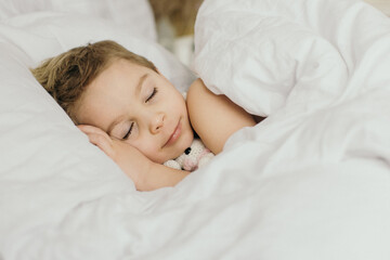 Beautiful blond toddler child, boy, sleeping in bed with teddy bear toy