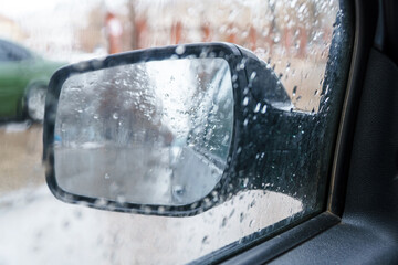 View of the rear view mirror on a rainy day from inside the car. Blurred view