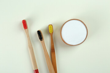Bamboo toothbrushes and bowl of baking soda on beige background, flat lay