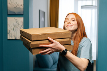 Portrait of enjoying young woman with closed eyes hugging boxes of hot pizza standing at entrance...