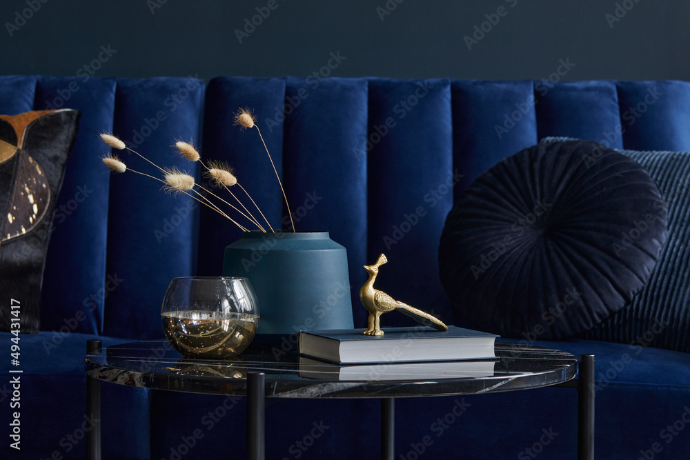 Wall mural Stylish and elegant details in the glamour living room interior. Black coffee table and creative personal accesories. Dark blue sofa on the background. Template. Copy space.