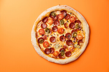 Pizza with smoked sausage, cherry tomatoes, dried chilli, jalapeno peppers and mozzarella. Orange background. Top view. Copy space