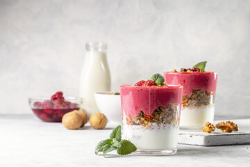 Yogurt, raspberry smoothie and homemade granola in a transparent glass. Healthy breakfast or snack. Copy space