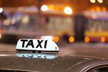 Shining Taxi inscription close up against passing cars on night street of big cit