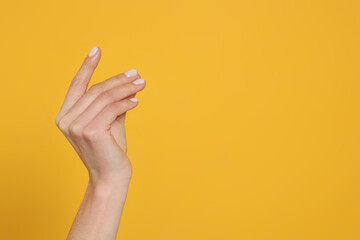 Woman holding something against yellow background, closeup on hand. Space for text
