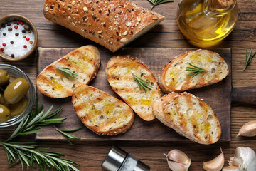 Tasty bruschettas with oil and rosemary on wooden table, flat lay