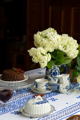 Table with blue embroidery tablecloth. Chocolate cake and flowers. Table on the street near the house