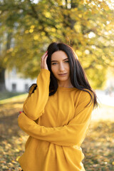 Beautiful woman in an orange sweater on a background of autumn foliage. Portrait of a joyful woman playing with leaves in the park in autumn.