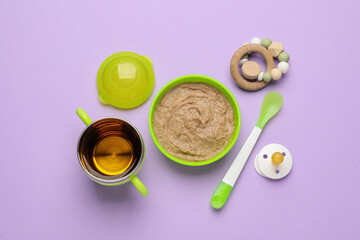 Obraz na płótnie Canvas Healthy baby food in bowl and accessories on violet background, flat lay