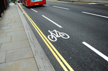 Fietspad met fietssymbool in de straten van Londen, VK en rode bus. Ecologisch en duurzaam vervoer. Energiebesparend. Wit fietspictogram op zwarte asfalttextuur. Stedelijke scène