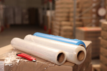 Rolls of different stretch wraps and utility knife on boxes in warehouse