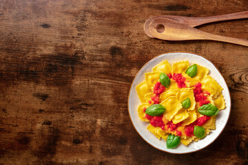 Ravioli with red tomato sauce and basil, overhead flat lay shot with copy space. Vegan Italian cuisine, on a rustic wooden background