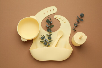 Flat lay composition with baby feeding accessories and bib on brown background