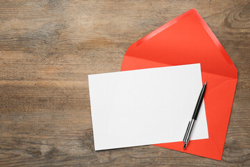 Envelope with blank paper card and pen on wooden table, top view. Space for text