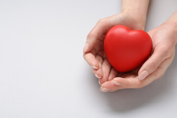 Woman holding red decorative heart on light grey background, closeup with space for text. Cardiology concept