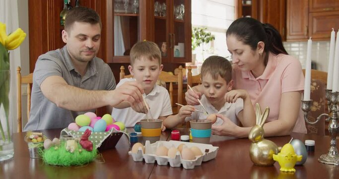 a family paints Easter eggs, father two siblings and mother