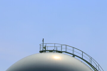 青空とガスタンクを望遠で写す。ガスタンクの球体と階段は、まるでコンビナートの様です。Take a telephoto shot of the blue sky and the gas tank. The sphere and stairs of the gas tank are like a complex. - obrazy, fototapety, plakaty