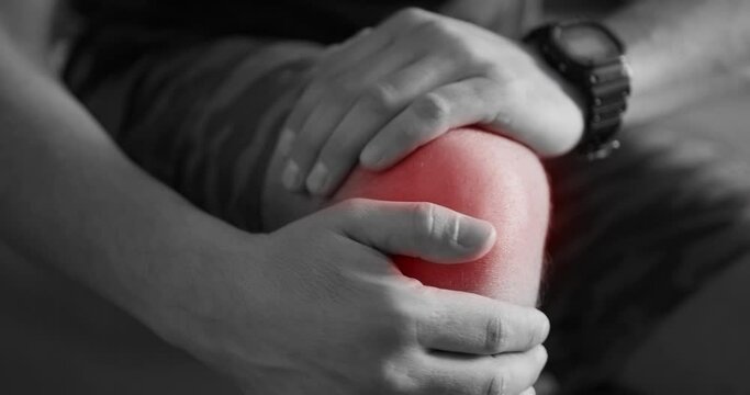 Black and white close up shot of men with knee injury severe pain holding on his foot