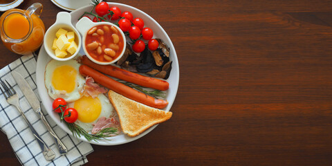 Banner Traditional full English breakfast fried eggs, sausages, beans, mushrooms, tomatoes, toasts, butter, jam, orange juice, bacon dark wooden background. Copy Space information, top view, Flat Lay