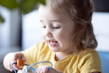 Fototapeta premium Close-up portrait of cute little girl playing with toy. Kid in yellow t-short excited game. 18-24 months kid. Learning and home education