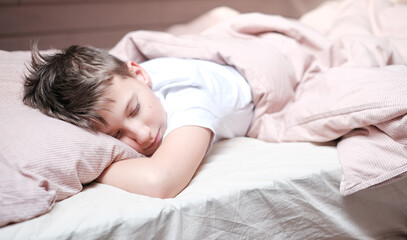 Obraz na płótnie Canvas Boy teen sleeping on the bed in morning. Beds blanket is in light pink colors