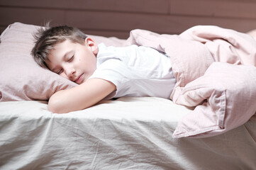 Boy teen sleeping on the bed in morning. Beds blanket is in light pink colors
