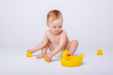 cute baby girl in a diaper playing with a rubber toy duck isolated on a white background