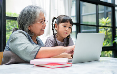 Asian Grandmother with her two grandchildren having fun and playing education games online with a...