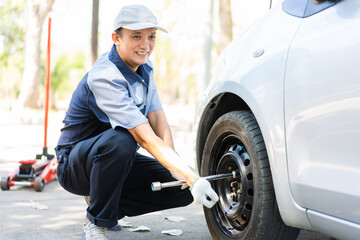 Expertise mechanic man  in uniform using force trying to unscrew the wheel bolts nuts and help a woman for changing car wheel on the highway, car service, repair, maintenance concept.